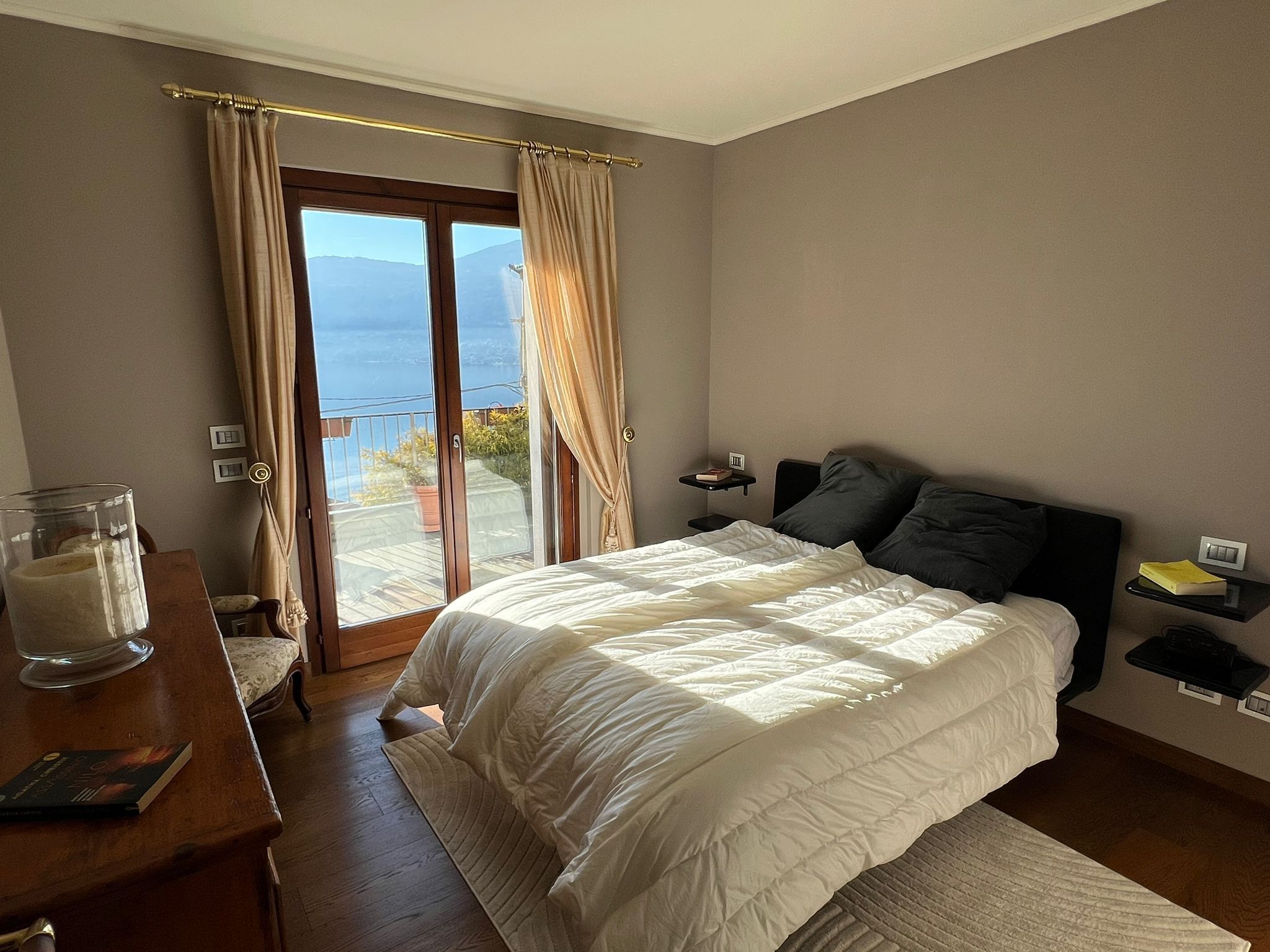 A bedroom with a bed, a bedside table, a nightstand, and a view of the outdoors through a sliding glass door.