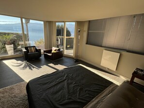 Un dormitorio con una cama grande, un sofá y una silla. Hay una ventana con vistas al mar y a las montañas.