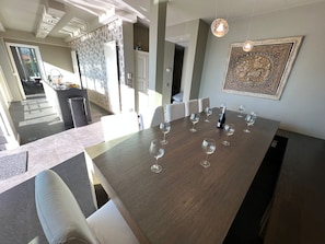 Un comedor con una mesa larga dispuesta para una comida, una cocina al fondo y un adorno en la pared.