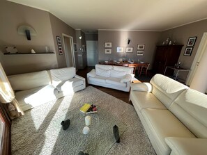 Una sala de estar con un sofá blanco, una mesa de centro con libros y un comedor al fondo.