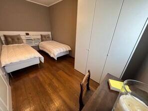Een kleine kamer met twee bedden, een houten vloer en een bureau met een stoel.