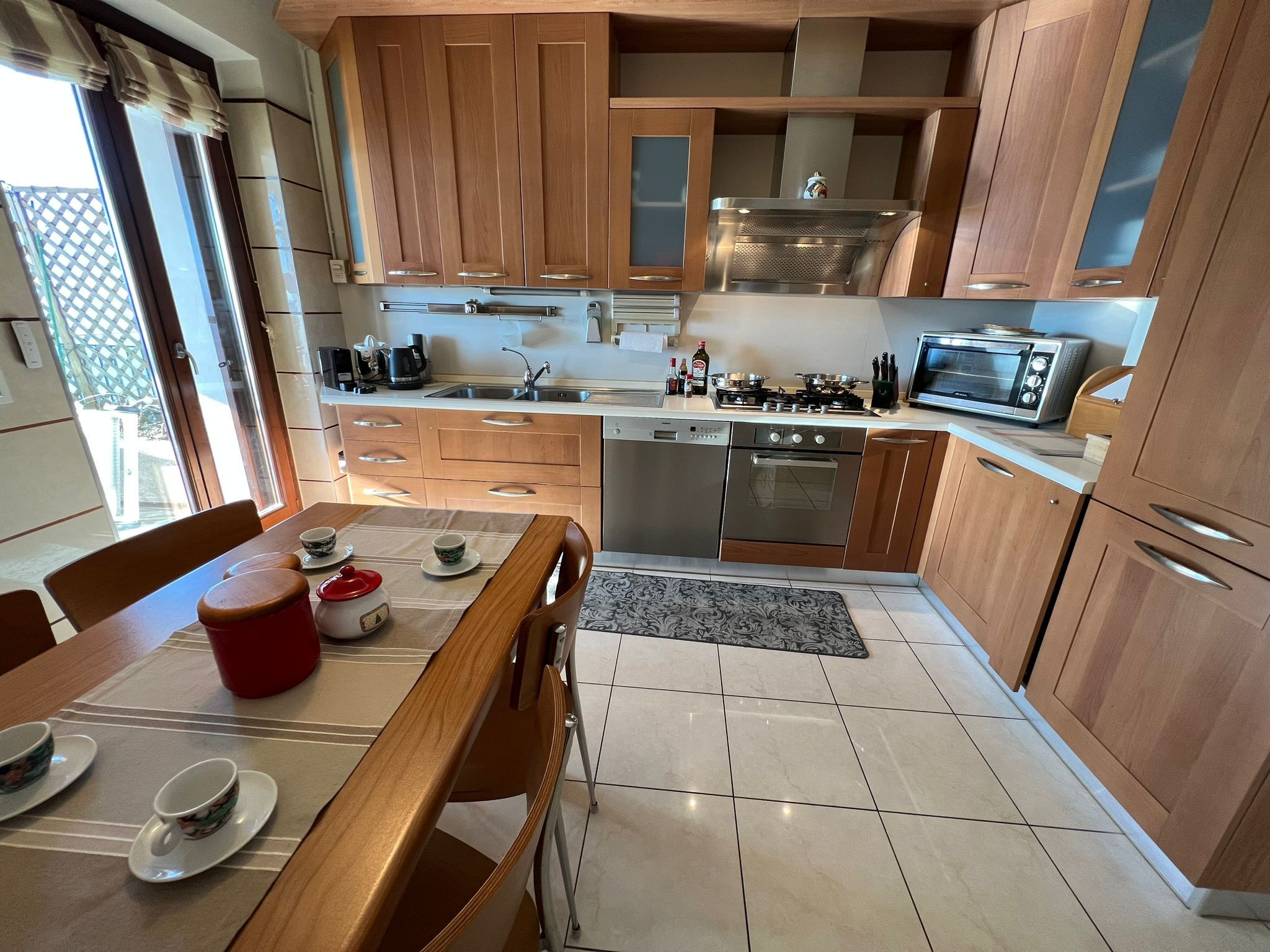 A compact kitchen with wooden cabinets, stainless steel appliances, and a dining area with a table set for two.