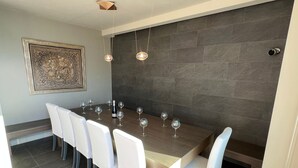 Un espace repas avec une longue table, des chaises blanches et de nombreux verres à vin.