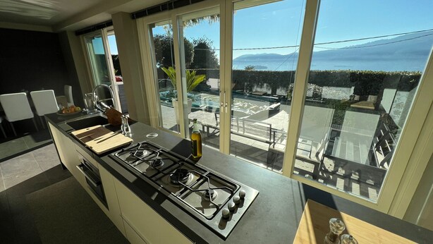 Une cuisine moderne équipée d’une cuisinière à gaz, de grandes fenêtres et offrant une vue sur une piscine et des montagnes.