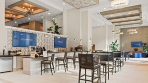 A modern hotel lobby with a reception desk, bar area, and seating.