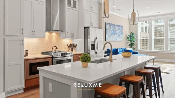 A modern kitchen with white cabinetry, a large island with stools, stainless steel appliances, and pendant lighting.