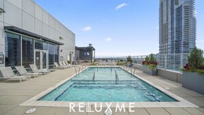 A rooftop pool with lounge chairs, a modern building, and a high-rise building in the background. - Reluxme | 2BR Condo in Center City w/ Spa Access (Charlotte)