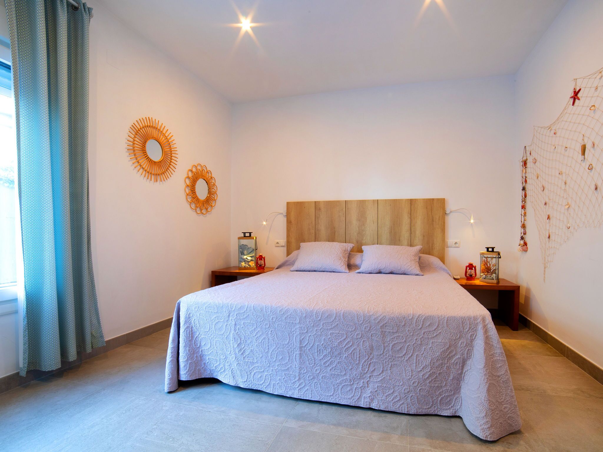 Ein ordentlich bezogenes Bett mit einem gemusterten Überwurf, zwei Wandleuchten und einem dekorativen Wandbild.