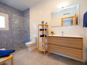A modern bathroom with a toilet, a wooden shelf with towels, a sink, and a mirror.