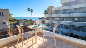 Ein Balkon mit Tisch und Stühlen, der Blick auf die Küste freigibt, mit einem Pool und modernen Gebäuden im Hintergrund.