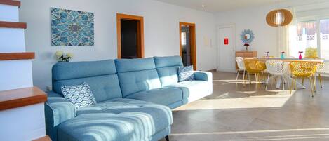Ein modernes Wohnzimmer mit einem blauen Ecksofa, einem Essbereich mit gelben Stühlen und einer Treppe mit Holzstufen.