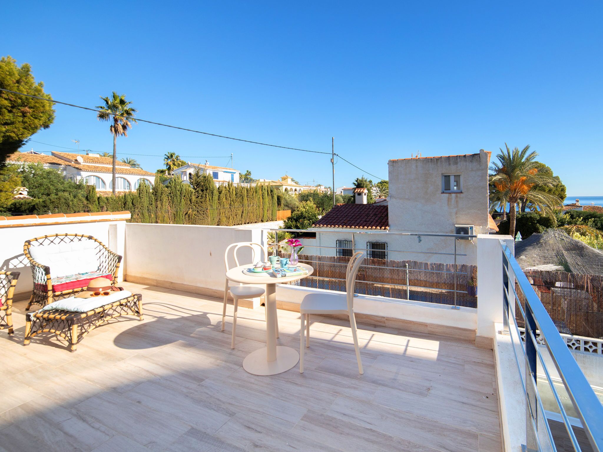 A balcony with a table and chairs, overlooking a coastal area with buildings and palm trees.