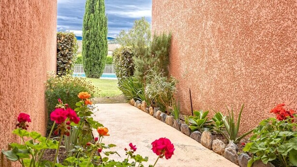A pathway flanked by pink and red flowers leading to a building with a textured facade. - Casarella Massari (Oletta)