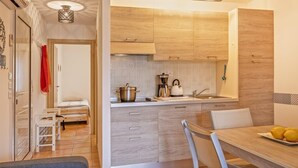 A modern kitchen with wooden cabinets, a sink, and a dining area with a table and chairs. - Casarella Massari (Oletta)
