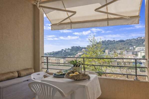 A balcony with a table and chairs, a view of a cityscape, and a white tablecloth. - Casa Sulana (Bastia)