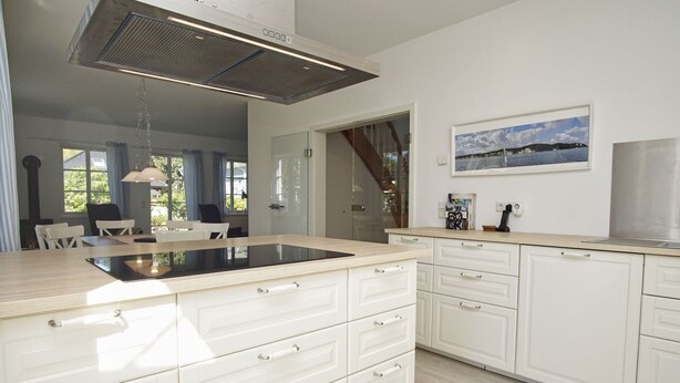 A modern kitchen with white cabinetry, a central island, and a large overhead vent.