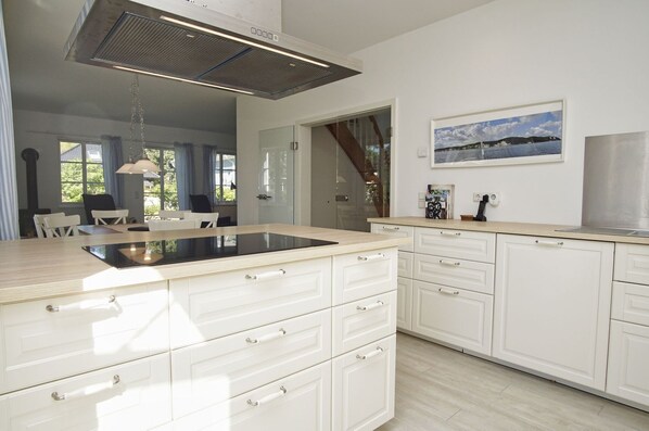A modern kitchen with white cabinetry, a central island, and a large overhead vent.