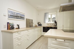 A modern kitchen with white cabinetry, a wooden countertop, and a large window with curtains. - Haus Schwedentraum - Gemütliches Haus mit Kamin, Sauna, Garten und Terrasse - Haus Schwedentraum (Wiek)
