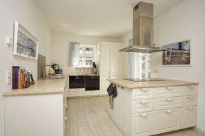 A compact kitchen with white cabinetry, a stainless steel range hood, and a window with curtains.