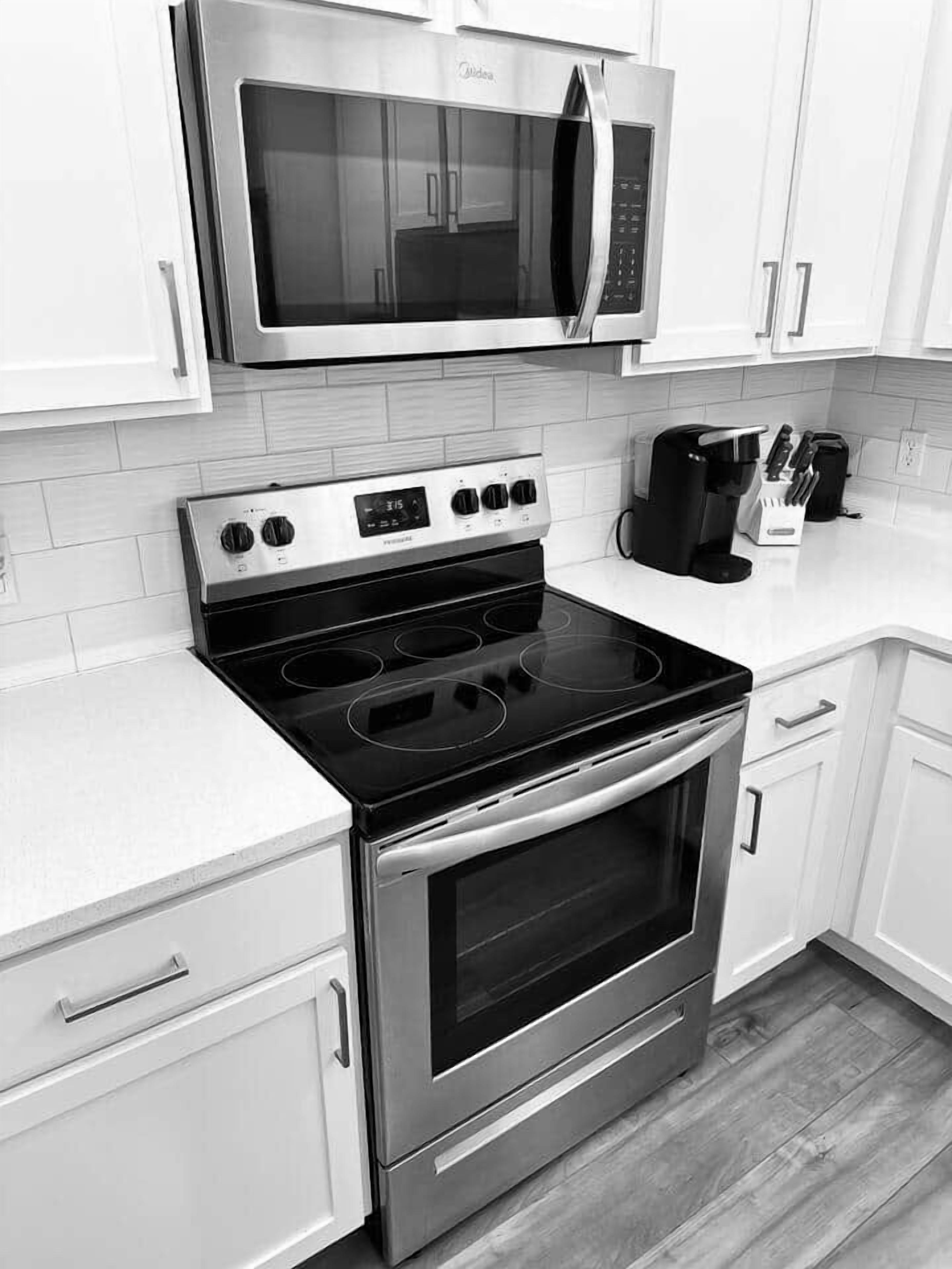 A kitchen with white cabinets, a stainless steel microwave, a stove with four burners, and a coffee maker.
