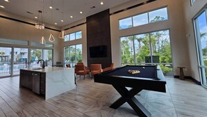 A modern indoor pool area with a pool table, seating, and large windows.