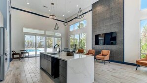 A modern kitchen with a large island, built-in appliances, and a dining area with orange chairs.