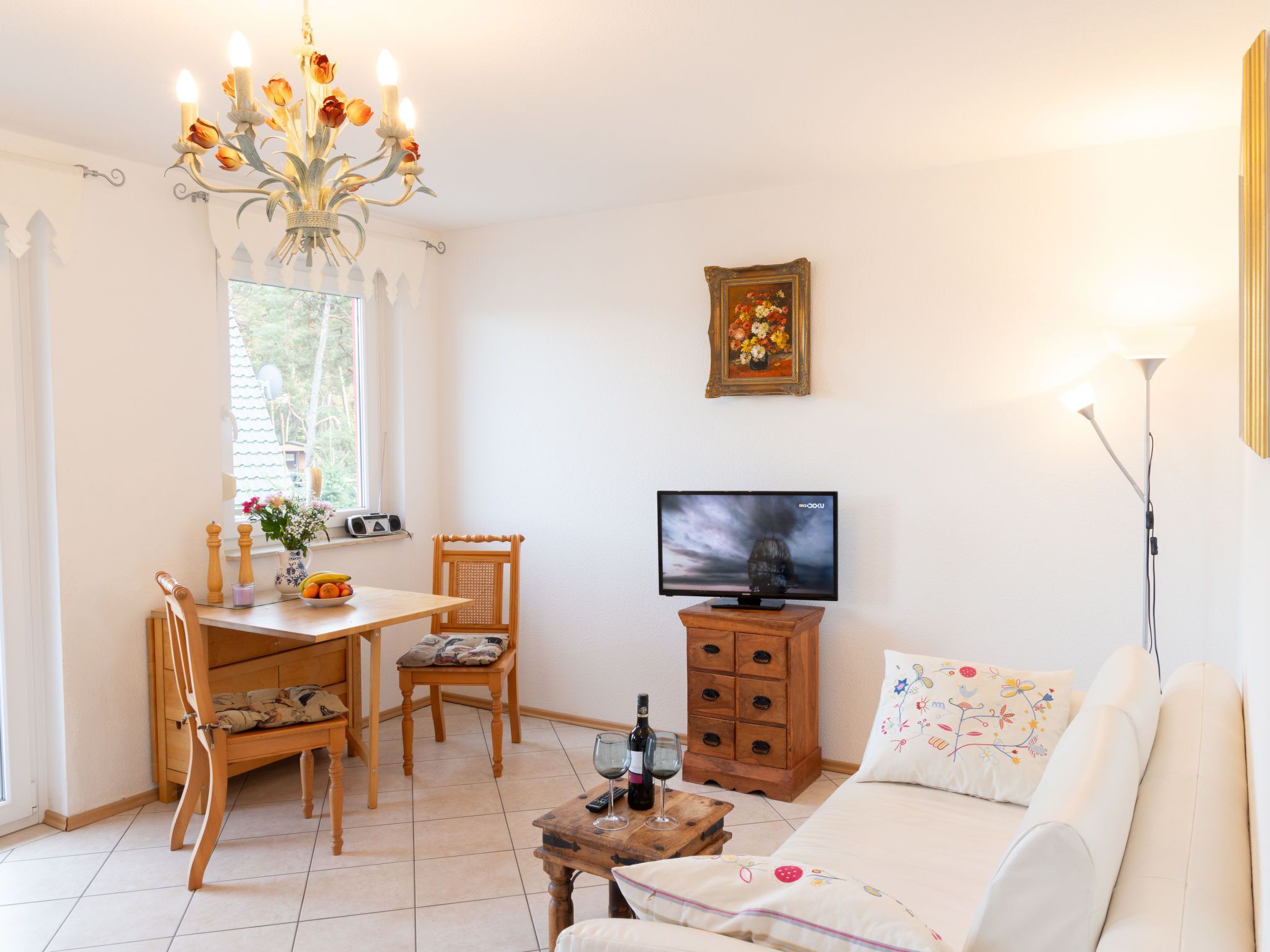 Ein gemütliches Wohnzimmer mit einem Holzesstisch, Stühlen, einer Couch, einem Fernseher und einer Pendelleuchte.