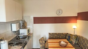 A compact kitchen with a microwave, kettle, and stove. There is a dining area with a table and chairs, and a clock on the wall. - Schmidt (App. 3) by Interhome (Zinnowitz)