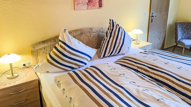 A neatly made bed with striped bedding, a bedside lamp, and a wall-mounted artwork. - Schmidt (App. 3) by Interhome (Zinnowitz)
