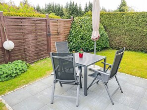 An outdoor patio with a table and chairs, a hanging lantern, and a neatly trimmed hedge in the background. - Schmidt (App.1) by Interhome (Zinnowitz)