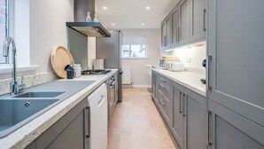Une cuisine moderne avec des meubles gris, un évier en acier inoxydable, une cuisinière à gaz et un four encastré.