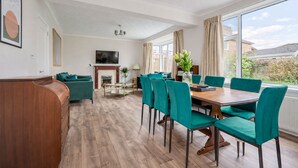Un salon spacieux doté d’une cheminée, un coin repas avec des chaises de couleur turquoise et une grande fenêtre offrant une vue sur l’extérieur.