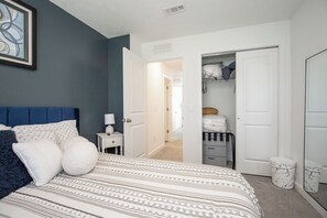 A bedroom with a bed, a nightstand, a closet, and a hallway.