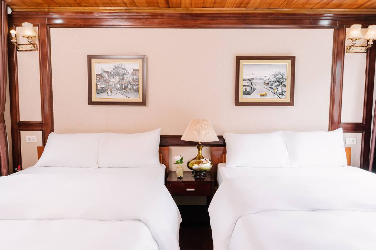 A hotel room with two beds, a nightstand with a lamp, and framed pictures on the wall.