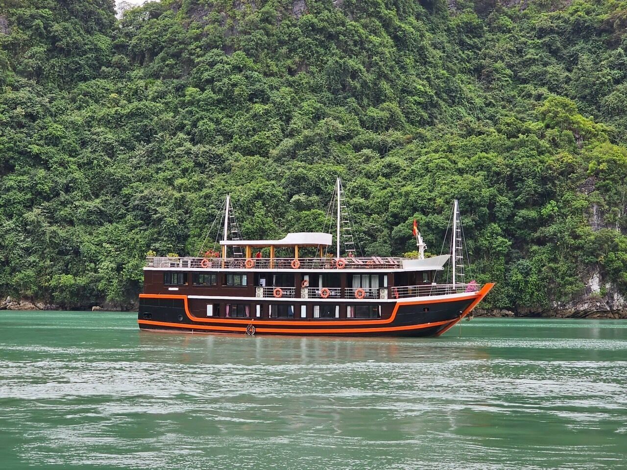 A riverboat with multiple decks, surrounded by dense green foliage.
