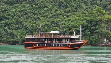 A riverboat with multiple decks, surrounded by dense green foliage.