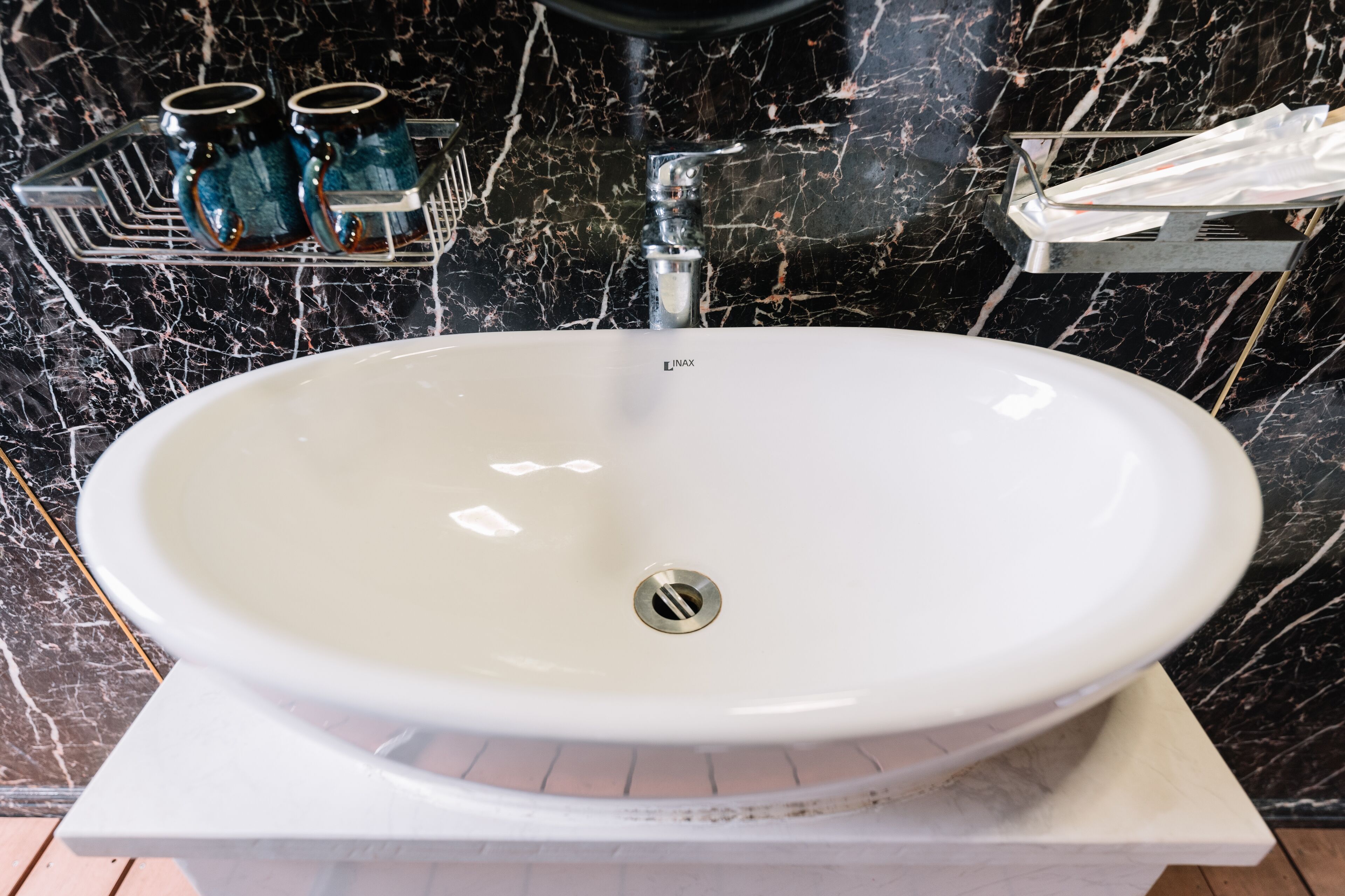 A white sink with a modern faucet, set against a black marble backsplash.
