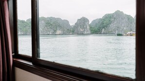 Blick aus einem Fenster auf ein Gewässer mit steinigen Klippen und einem Boot.