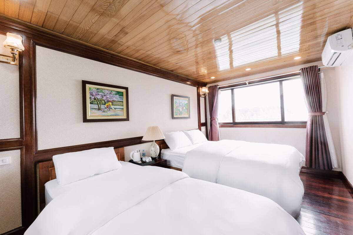 A hotel room with two beds, wooden ceiling, wall-mounted air conditioning, and framed artwork.