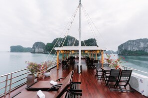 A deck with wooden furniture and potted plants, overlooking a body of water with rocky cliffs in the background. - Daiichi Boutique Cruise (Hai Phong)