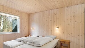Une chambre avec un grand lit, des murs en bois, une fenêtre et deux lampes fixées au mur.