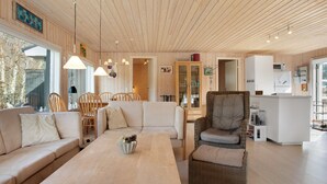 Un vaste espace de vie doté d’un plafond en bois, d’un ensemble de canapés, d’une table à manger et d’un fauteuil en osier.