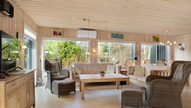 Un salon spacieux doté d’un plafond en bois, de grandes fenêtres et d’un coin salon confortable avec un canapé et des fauteuils.