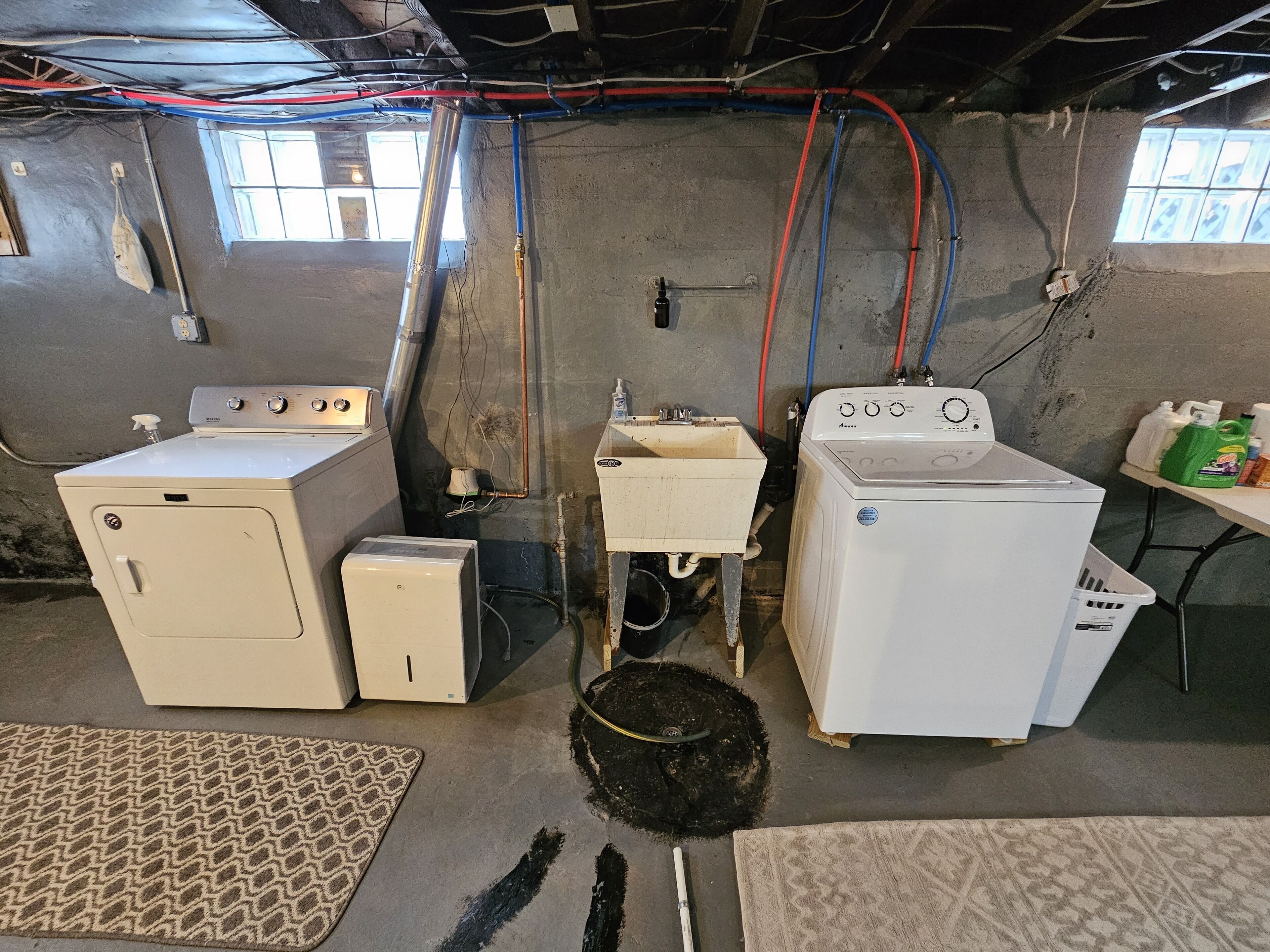 Une buanderie équipée de deux machines à laver, d’un petit sèche-linge et dont la tuyauterie est visible.