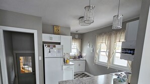 A modern kitchen with granite countertops, white cabinetry, and pendant lighting. - Becky's Bee Hive, Clean, Cozy, Affordable and Family Friendly! (Ironwood)