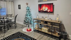A living room with a Christmas tree, a fireplace, a dining area, and a TV mounted on the wall. - Becky's Bee Hive, Clean, Cozy, Affordable and Family Friendly! (Ironwood)