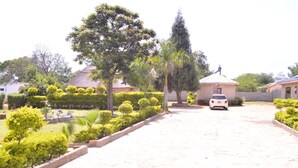 A paved driveway leading to a building with a thatched roof, surrounded by well-maintained hedges and trees. - Napier  Family-sized condo in Central Bulawayo (Bulawayo)