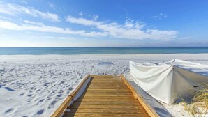 Ein hölzerner Steg führt zu einem Sandstrand, auf der rechten Seite steht ein Zelt.