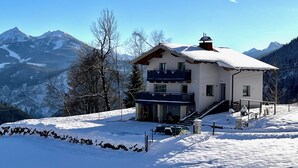 Ein zweistöckiges Chalet mit Balkon, vor einer verschneiten Berglandschaft.