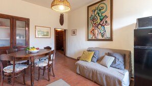 Un'area pranzo con un tavolo e sedie in legno, un lampadario a sospensione, un quadro appeso al muro e un divano con cuscini.